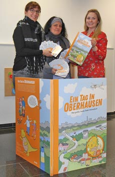 Bild: Die KIM-Mitarbeiterinnen Natascha Beulshausen (li.) und Fatma Kurt-Ayar (Mitte) sowie Eva Rogge (evo) mit dem aktuellen Wimmelbuch. (Foto:evo)
